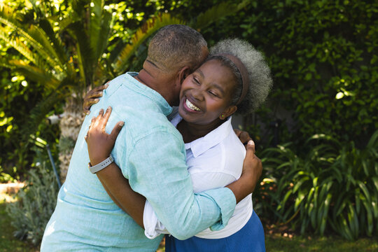 Senior couple embracing joyfully in lush garden, enjoying sunny day together