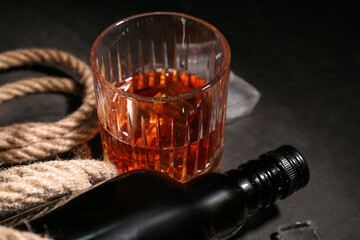 Bottle, glass of cold rum and rope on black grunge background