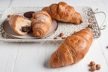Tray with sweet chocolate croissants and hazelnuts on white wooden background