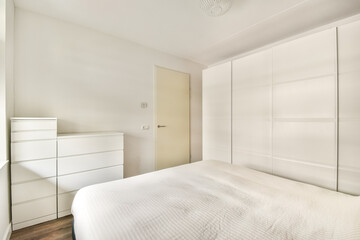 A modern minimalist bedroom featuring a white bed and dresser, emphasizing simplicity and clean lines. The design promotes a serene and organized atmosphere.