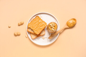 Jar with tasty peanut butter, wooden spoon, toasts and nuts on beige background