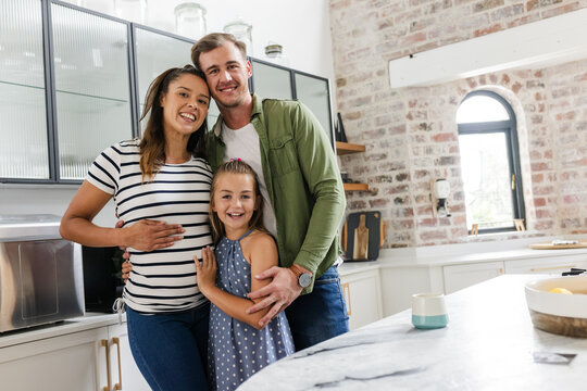 Happy family in kitchen, parents embracing daughter, enjoying time together at home