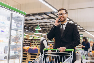 Businessman talking on phone and pushing shopping cart in supermarket