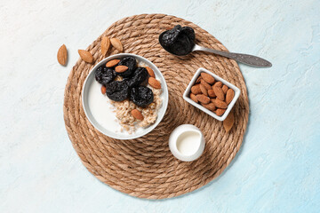 Bowl of tasty oatmeal with prunes, almonds and milk on light background