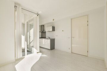 A spacious, minimally furnished room featuring a modern kitchen and large windows that allow natural light to flood the space. The design emphasizes simplicity and elegance.