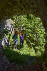 Women hiking past forest cave opening