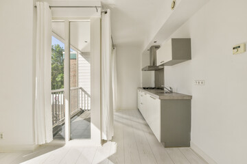 A clean, modern kitchen interior featuring white walls, sleek cabinetry, and large windows that invite natural light.