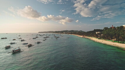 Aerial view capturing Cagban Beach at sunset, featuring traditional Philippine bangkas floating on turquoise waters alongside lush greenery and white sand, Boracay Island