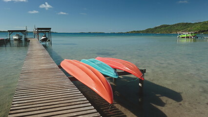 Wooden pier, crystal clear turquoise water, three vibrant kayaks, orange and light blue, secured to...