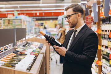 Businessman choosing wine in supermarket, reading label on bottle