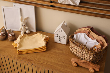 Baby clothes with toys on chest of drawers in room
