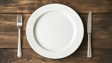 Empty white plate with cutlery on wooden table.