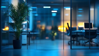 Modern office interior with glass walls plant and blurred background at night.