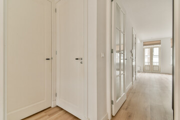 A spacious and modern interior hallway featuring light-colored walls, wooden flooring, and windows allowing natural light to brighten the space.