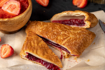 puff pastry with filling and strawberries, a puff pastry bun with strawberry and cherry flavor lies on paper, close up