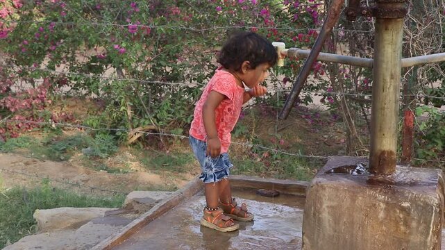 18 months old baby operate the traditional handpump , drinking water and enjoying with water in summer 