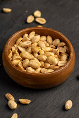 peanuts in a wooden round bowl, crunchy peanuts without shells on a black slate board, close up