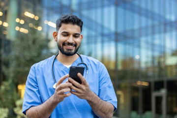 A smiling doctor checks his phone, possibly viewing patient records or communicating with colleagues, outdoors.