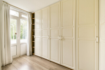 Spacious interior featuring white cabinets, natural light from windows, and a warm wooden floor, creating an inviting atmosphere for any room.
