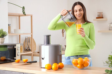 Young woman with modern juicer pouring orange juice in kitchen
