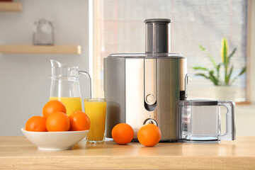 Modern juicer with oranges on table in kitchen