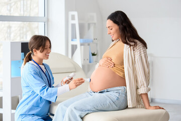 Fototapeta premium Young pregnant woman and doctor with fetal doppler listening to baby's heartbeat in clinic