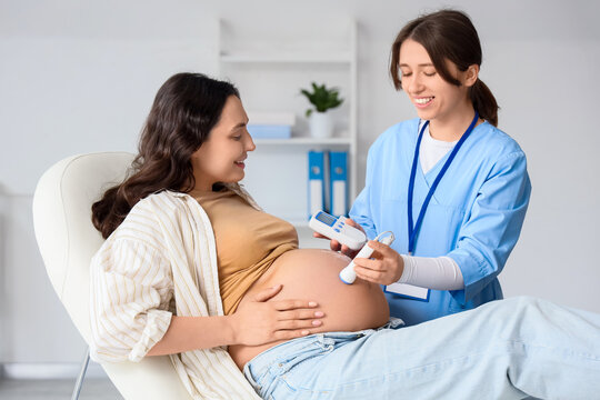 Young pregnant woman and doctor with fetal doppler listening to baby's heartbeat in clinic