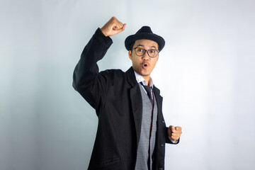 Asian man dressed as mafia wearing glasses and hat, celebrating victory with an excited expression