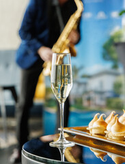 Close-up of a champagne flute and tray of meringue pastries with blurred saxophone player in the background