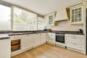 A spacious modern kitchen featuring white cabinets, granite countertops, and ample natural light through large windows, showcasing a minimalist aesthetic.