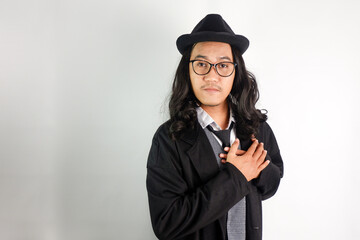 long haired asian man dressed as mafia wearing glasses and hat, making a gesture of holding his...