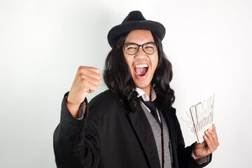 Asian man with long hair dressed as a mafia wearing glasses and a hat with an exited face holding a...