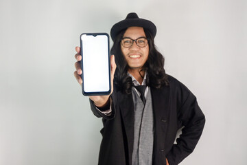 Asian man with long hair dressed as a mafia wearing glasses and a hat showing a smartphone with a blank screen and his face smiling