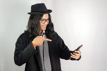 Asian man with long hair dressed as a mafia wearing glasses and a hat holding a smartphone and the...