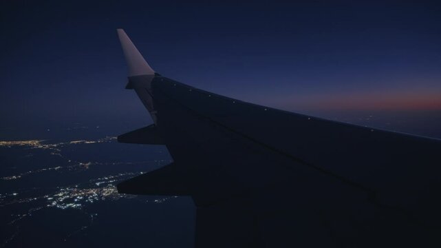 Enjoy the stunning night view from an airplane descending to a city, aglow with vibrant, twinkling lights creating an enchanting atmosphere