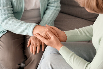 Mature woman with her mother holding hands on sofa at home, closeup
