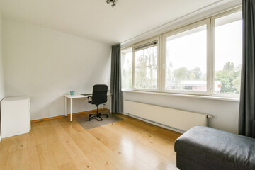 A spacious and well-lit home office featuring a simple desk, a comfortable chair, large windows, and a cozy atmosphere. Ideal for productivity and relaxation.