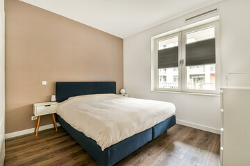 A contemporary bedroom featuring a cozy bed with a simple design, wooden flooring, and a large...