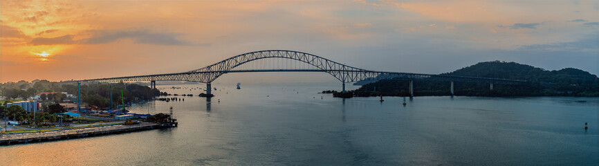 A panorama view from a ship sailing under the Bridge of the Americas towards the Panama Canal entrance in Panama at sunrise in springtime