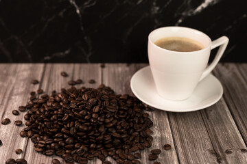 A cup of coffee and coffee beans on a dark background. Roasted coffee beans.