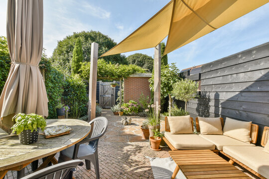 A beautifully arranged outdoor garden patio featuring comfortable seating, vibrant greenery, and a stylish shade sail, perfect for relaxation and gatherings.