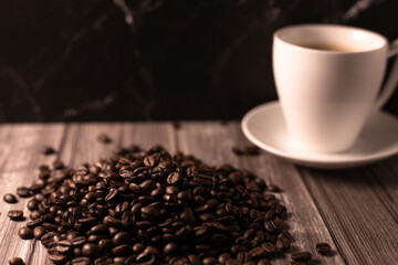 A cup of coffee and coffee beans on a dark background. Roasted coffee beans.