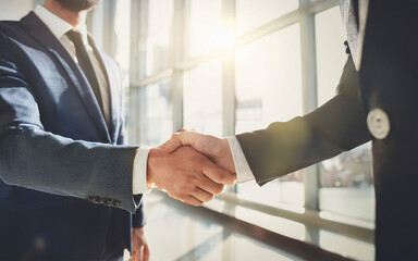 Dos profesionales de negocios dándose la mano en una oficina moderna, simbolizando el cierre de un acuerdo exitoso. La escena transmite confianza, profesionalidad y cooperación. Estilo fotorealista