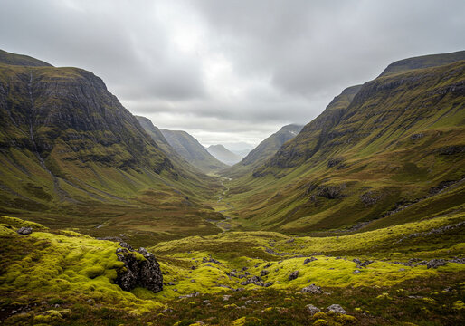 Mountain Valley Landscape with Green Moss and Cloudy Sky in Scotland. The mountain valley is surrounded by mountains with a river running through it under cloudy sky