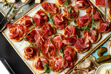Top view of a rustic platter featuring assorted tapas topped with thinly sliced prosciutto, garnished with herbs