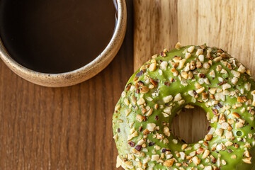 top view of cup of fresh aromatic coffee and glazed pistachio  donut on wooden cutting board close...