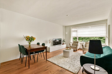 A stylish modern living space featuring a wooden dining table, green chairs, and natural light from large windows. The room has an elegant and cozy atmosphere.