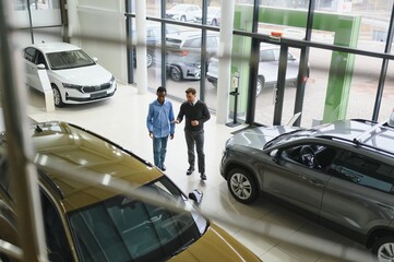 Car Sales Manager Showing Auto To Buyer Standing In Luxury Automobile Dealership Store