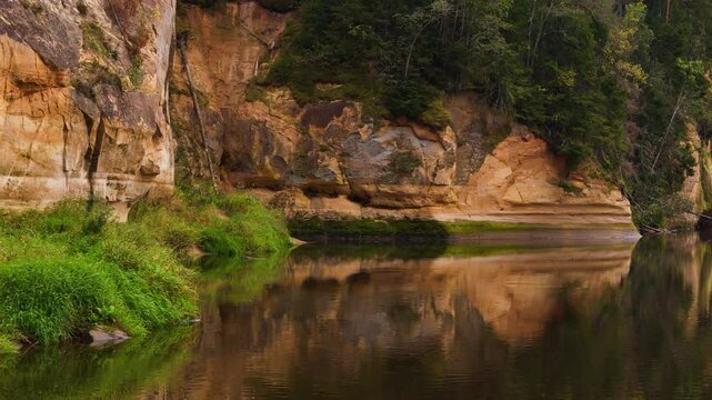 Horizontal sandstone layers reflected in the calm Gauja River at Erglu Cliffs in Latvia.