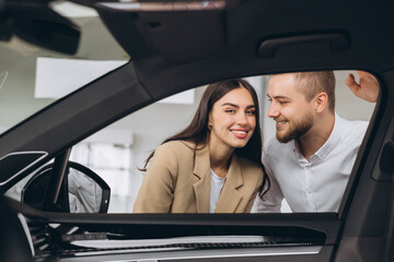 Cheerful young man and woman buying new car, checking automobile salon through window, panorama....